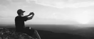 Young man sitting on rock taking photo